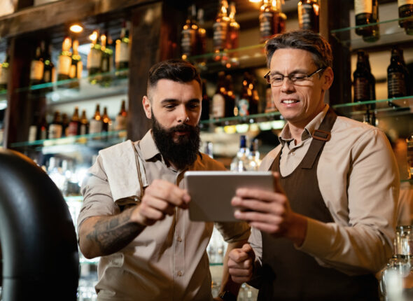 Two bartenders using digital tablet while working in a bar.